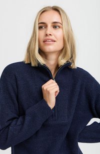 Námornícky modrý fleece pulóver s polovičným zipsom, ribbed textúrou, voľným strihom a dlhými rukávmi. Mäkký materiál, minimálne dekoratívne prvky.