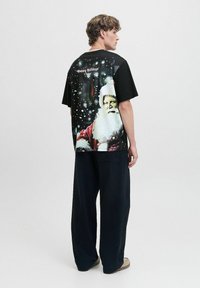 Sort T-shirt med et levende Santa Claus grafik, snefnug og teksten "Glædelig Jul" på ryggen. Bred, afslappet pasform.