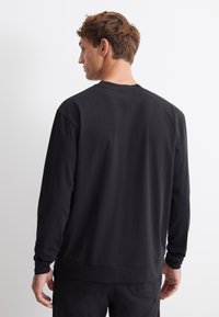Zwarte lange mouwen sweatshirt van katoen, met een ronde hals, ribgebreide manchetten en een ontspannen pasvorm, gezien vanuit de achterkant.