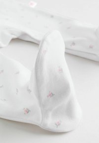 Hvide småbørnsstrømper med en blød bomuldsblanding, dekoreret med små lyserøde og grå blomsterprint og en glat tekstur.