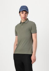 Πολυ είτε ριγέ γαλάζιο και λευκό με λαιμόκοψη, σε ελαιόχρωμο, και με μικρό λογότυπο στο στήθος; επίπεδο ύφασμα και κοντά μανίκια.