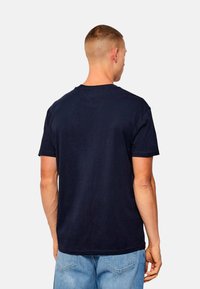 Camiseta de algodón azul marino con mangas cortas, un cuello redondo clásico y un corte holgado, mostrada desde la parte trasera sin gráficos visibles.