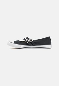 Zapato plano de lona negra con dos correas con hebillas, punta de goma blanca y suela a rayas en blanco y negro. Diseño elegante y de perfil bajo.