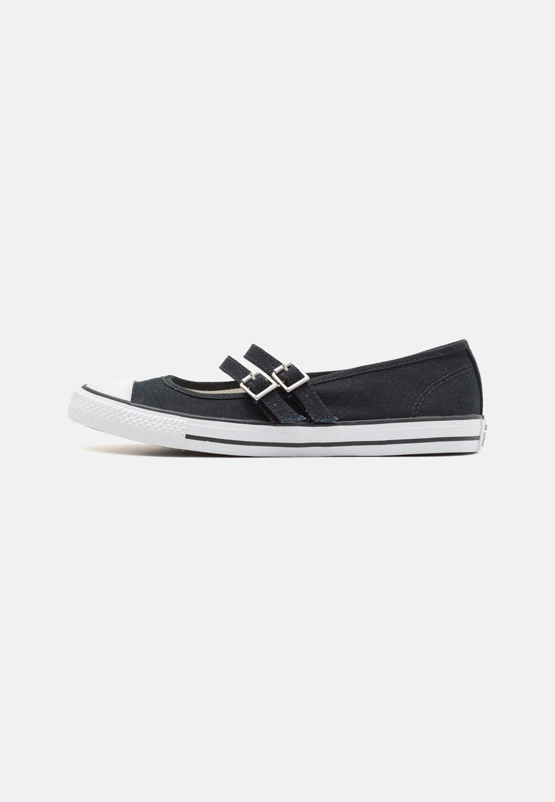 Zapato plano de lona negra con dos correas con hebillas, punta de goma blanca y suela a rayas en blanco y negro. Diseño elegante y de perfil bajo.