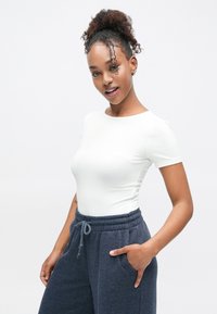 White short-sleeve top paired with navy sweatpants featuring an elastic waistband and side pockets. Smooth texture; casual fit.