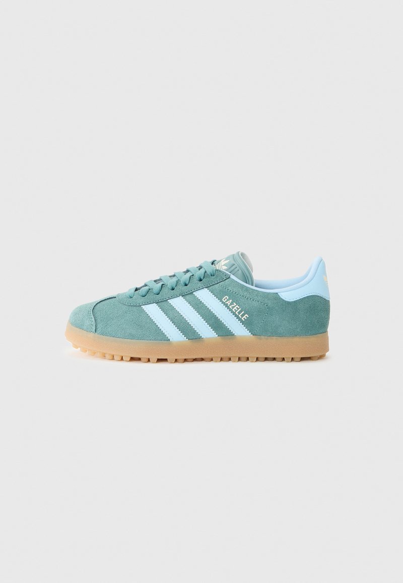Baskets en daim vert avec trois rayures bleu clair, étiquetées "Gazelle." Elles présentent une semelle texturée et une doublure intérieure douce bleu.