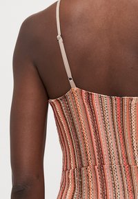 Multicolored striped top featuring thin beige straps, textured fabric with patterned stitching, and a fitted design.