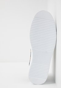 Semelle de sneaker blanche avec des rainures texturées ; partie supérieure noire avec des accents orange ; surface lisse ; design minimaliste.