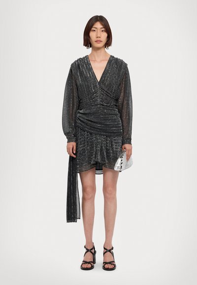 Black, textured mini dress with ruched detail, long sleeves, a deep v-neckline, and a side tie. Paired with a metallic clutch and black sandals.
