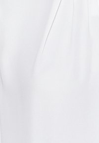 Witte blouse van zachte, gladde stof met subtiele plooidetails langs de halslijn, wat zorgt voor een zachte draping.