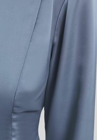 Satin klänning i ljusblått med en slät textur, med en figursydd överdel och vida ärmar, som framhäver subtil sömnadsdekor.