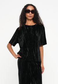 Haut en velours noir écrasé à manches courtes, avec un col rond et une coupe ample, associé à un pantalon noir assorti.