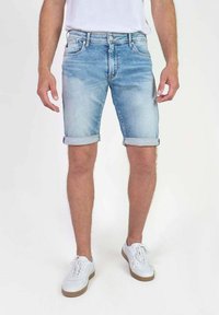 Bermudas de denim azul claro con puños enrollados, diseño de cinco bolsillos y detalles de costura. Combinadas con zapatillas blancas y una camiseta básica.