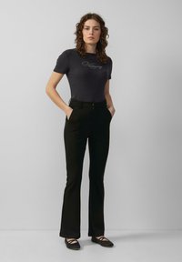 Donkergrijze korte mouwen rib t-shirt met geborduurde tekst, gecombineerd met zwarte strakke flared broeken. Het schoeisel bestaat uit zwarte ballerina's.
