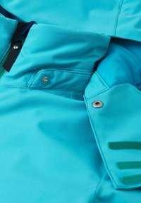 Türkisfarbene wasserdichte Jacke mit glatter Textur, ausgestattet mit metallischen Druckknöpfen, einer Reißverschlusstasche und kontrastierenden grünen Klettverschlüssen an den Ärmeln.