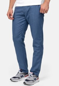 Pantalones de algodón azul con un corte ajustado, que incluyen bolsillos laterales y una textura suave. Combinados con zapatillas deportivas grises y marinas.