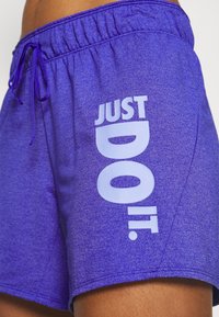 Fialové sportovní šortky s elastickým pasem a šňůrkou, s nápisem "JUST DO IT." vytištěným vertikálně na levé stehně.