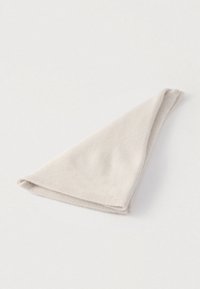 Tissu doux beige clair plié reposant sur une surface blanche, arrangé en forme triangulaire.