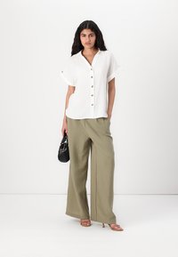 Camicia bianca con maniche arrotolate, abbinata a pantaloni larghi verde oliva. Sono inclusi una borsa nera e sandali con cinturini rosa chiaro.