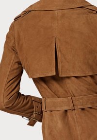 Detalj av baksidan på en brunt mocka trenchcoat, inklusive ventilerad klaff, bälte med spänne och ärmslut med bälte på lång ärm.