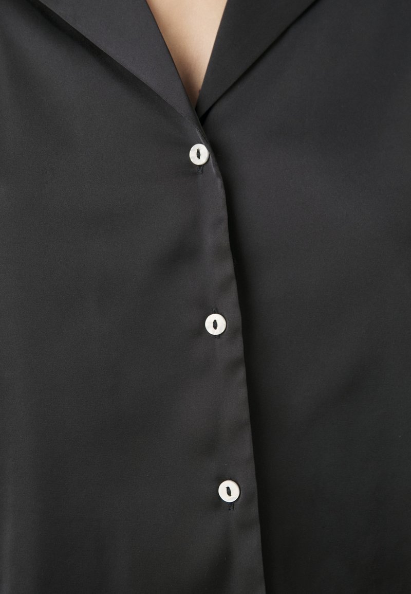 Camisa de satén negra con cuello clásico, cierre de seis botones con botones blancos y textura suave.