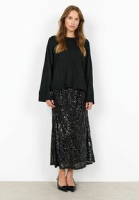 Czarny, oversize sweter z długimi rękawami w połączeniu z długą, czarną spódnicą wysadzaną cekinami. Całość charakteryzuje się gładkimi fakturami i błyszczącym wykończeniem.