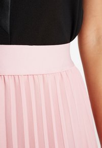 Musta yläosa ja poimutettu vaaleanpunainen hame. Vyötäröosa on leveä ja teksturoitu, kun taas hame on kevyttä materiaalia ja siinä on pystysuoraan taitoksia.