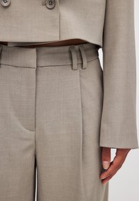 Heled hall ülikond, millel on lühike jakk topelt nuppe ja volditud püksid koos küljetaskute ja vöökandmistega. Tekstuuriga kangas.