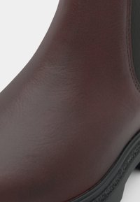 Bordeauxfärgade läderankelboots med en slät yta, elastiska sidopaneler och en svart gummisul med ett lätt mönster.
