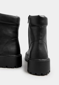 Botas de tobillo de cuero negro con un acabado texturizado, cierre de cremallera y suelas de goma gruesas con un intenso dibujo para mayor tracción.