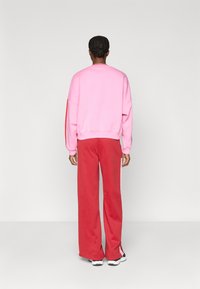 Rózsaszín, oversized kapucnis pulcsi, piros, bő szárú nadrág fehér oldalsávokkal, laza szabás, pamutkeverék anyag, sima textúra.