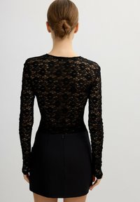 Top de encaje negro de manga larga con patrón floral, de corte ajustado y escote redondo, combinado con una falda mini negra con cremallera.