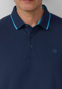 Marineblaue Poloshirt mit strukturiertem Finish, kontrastierender türkisfarbener Kragenverzierung, Knopfleiste mit drei Knöpfen und kleinem blauen Logo auf der Brust.