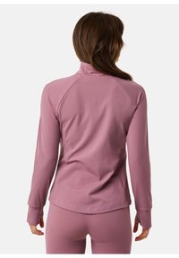 Long-sleeve athletic top in light pink fabric, featuring a high collar, raglan sleeves, and smooth texture. Designed for comfort and movement.