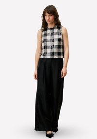 Zwart-wit geruit mouwloos topje met een glanzende afwerking, gecombineerd met zwarte, hooggetailleerde, wijd uitlopende broek en zwarte puntige schoenen.