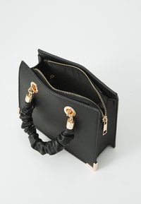 Sac en cuir noir à la forme structurée, avec des détails dorés et une anse souple froncée. Il dispose d'une fermeture éclair et de poches intérieures.