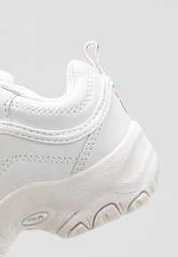 Baskets blanches avec une semelle en caoutchouc texturé, tige en cuir lisse et couture contrastante. Elles présentent une languette au talon et un détail de logo.