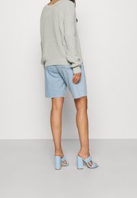 Jasnoszary, oversize, dziany sweter, niebieskie, postarzane szorty dżinsowe oraz jasnoniebieskie sandały na blokowym obcasie z plecionymi paskami.