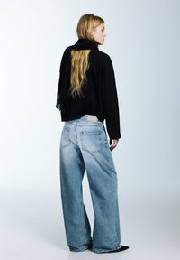 Černý zkrácený svetr s třásněmi, kombinovaný se světle modrými džínami s širokými nohavicemi. Oblečení má jednoduchý, pohodlný střih.