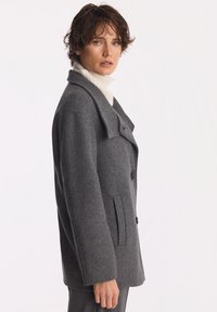 Szary płaszcz wełniany z klapami, bocznymi kieszeniami i dwoma guzikami, o luźnym kroju.
