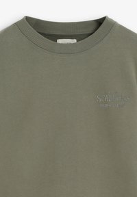 Sudadera verde oliva hecha de algodón suave, con un cuello de canalé y un logo bordado en el pecho en un color contrastante.