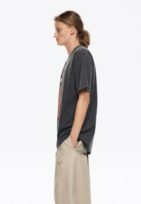 Camiseta gris de gran tamaño con un estampado gráfico, mangas cortas y un ajuste relajado, combinada con pantalones cortos de un beige claro.