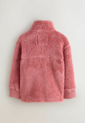 Skats no aizmugures uz mīkstu rozā vilnas jaku ar ribām ap kakla un aproču galiem, uz vienkārša fona.