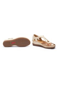 Sandalias de piel beige con diseño recortado, acentos trenzados y un bajo tacón cuña marrón; suela de goma texturizada con un dibujo en el revestimiento.