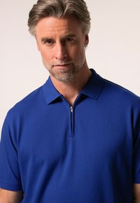 Modrá polo košile se zipovým límečkem, texturovaná tkanina a jemná logo detail. Krátké rukávy a přiléhavý střih.