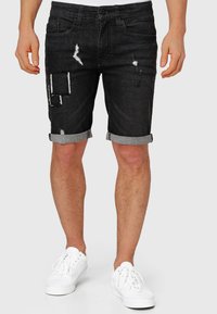 Pantaloni scurți din denim negru cu detalii uzate, inclusiv pete rupte și tivuri destrămate. Manșete rulate și design clasic cu cinci buzunare.