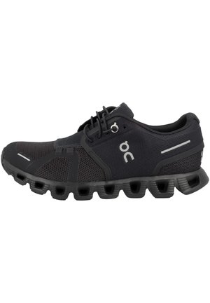 Czarne buty sportowe z oddychającej siateczki, gumowa podeszwa z okrągłymi wycięciami i odblaskowymi akcentami po bokach.