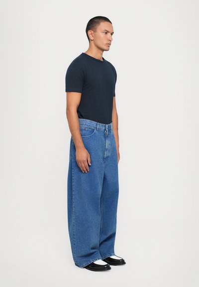 Mörkblå t-shirt med kort ärm som kombineras med oversize ljusblå jeans och svarta skor. Jeans har en klassisk femfickdesign.