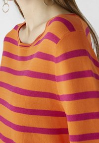 Pull orange avec des rayures horizontales rose foncé. Col bateau et tricot texturé. Gros plan sur le motif et le tissu.