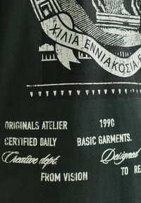 Melnā T-kreklā ir balti drukāti teksti un grafikas, tostarp logotips, dizaina elementi un tipogrāfija dažādos stilos un izmēros.